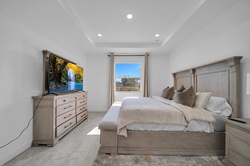 Spacious primary bedroom suite in the Madison model home by Paladium One in LaBelle, Florida, featuring a king bed, tray ceiling with recessed lighting, dresser with TV, and carpet flooring.