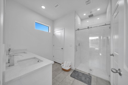 Modern primary bathroom in the Madison model home by Paladium One in LaBelle, Florida, featuring a white vanity with quartz countertop, a walk-in shower with glass enclosure, and a small window for natural light.